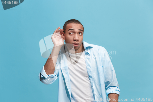 Image of The young man whispering a secret behind her hand over blue background