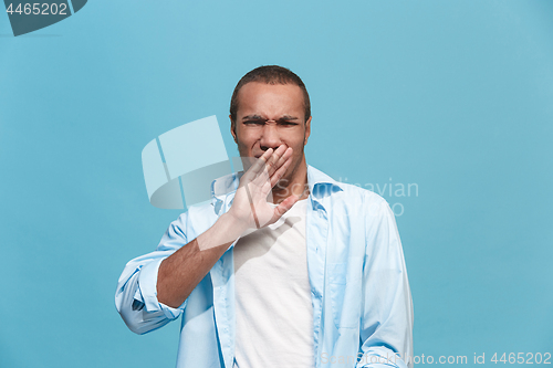 Image of Young man with disgusted expression repulsing something, isolated on the blue