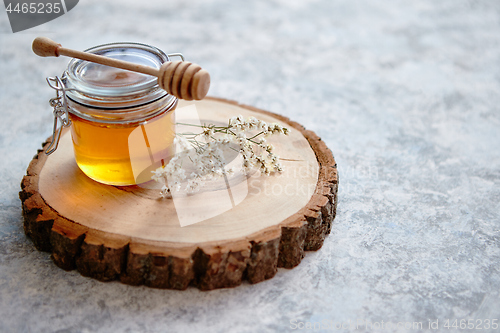 Image of Glass jar full of fresh honey placed on slice of wood