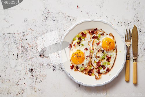 Image of Two fresh fried eggs with crunchy crisp bacon and chive served on rustic plate