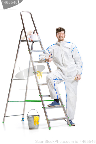 Image of Young male decorator painting with a paint roller climbed a ladder isolated on white background.