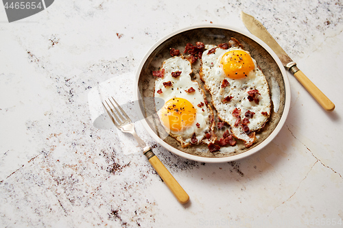 Image of Two fresh fried eggs with crunchy crisp bacon served on rustic plate