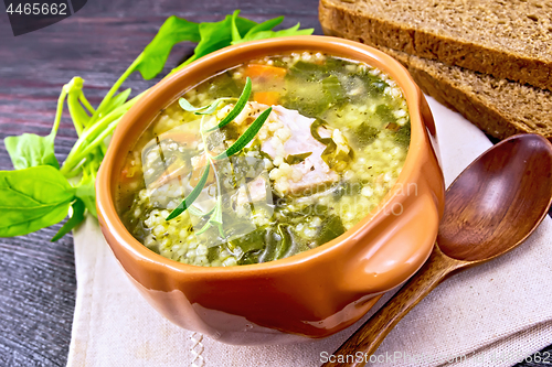 Image of Soup with couscous and spinach in clay bowl on wooden board