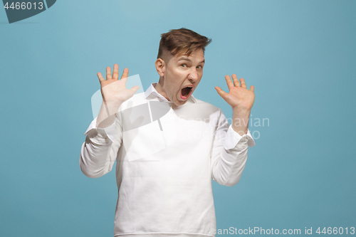 Image of The young emotional angry man screaming on blue studio background