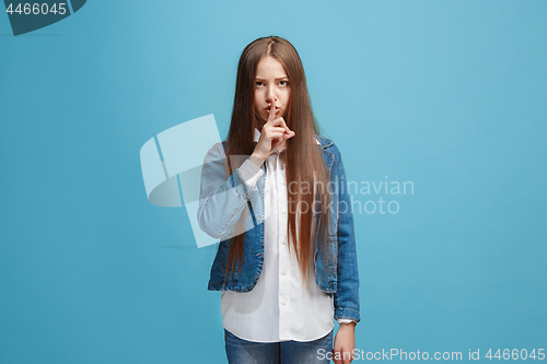 Image of The young teen girl whispering a secret behind her hand over blue background