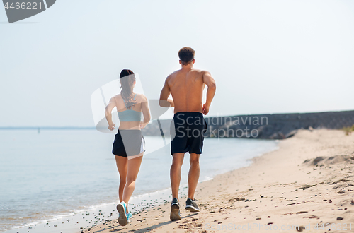 Image of couple in sports clothes running along on beach