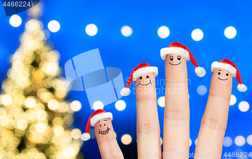 Image of fingers in santa hats over christmas tree lights