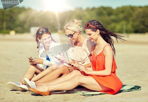 Image of group of happy women with smartphones on beach