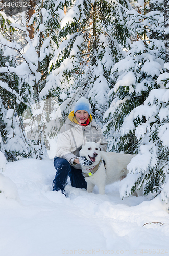 Image of Joyful woman with a white dog in the winter snow-covered forest