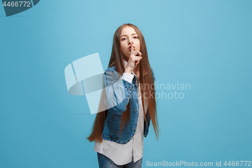 Image of The young teen girl whispering a secret behind her hand over blue background