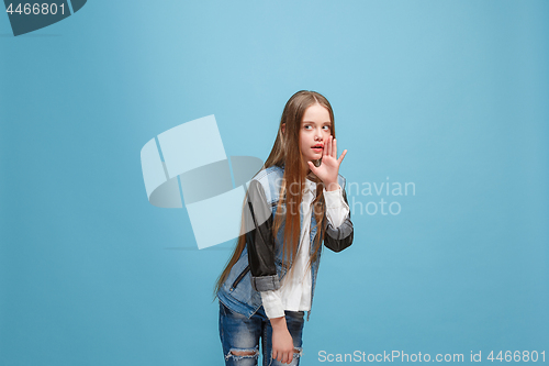 Image of The young teen girl whispering a secret behind her hand over blue background