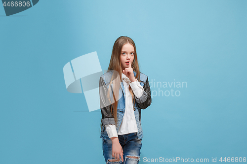 Image of The young teen girl whispering a secret behind her hand over blue background