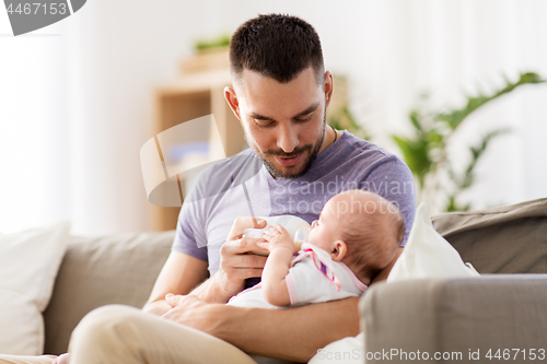 Image of father feeding baby daughter from bottle at home