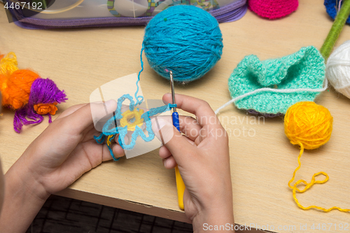 Image of The girl knits a flower from thread, close-up