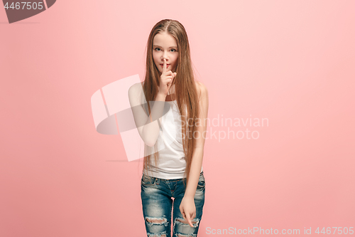 Image of The young teen girl whispering a secret behind her hand over blue background