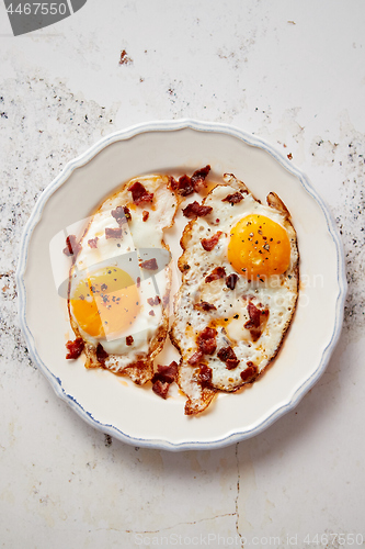 Image of Two fresh fried eggs with crunchy crisp bacon and chive served on rustic plate