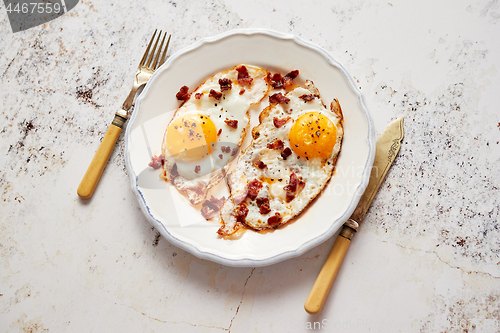 Image of Two fresh fried eggs with crunchy crisp bacon and chive served on rustic plate