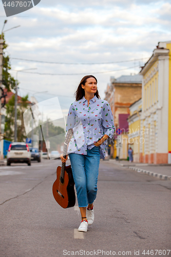 Image of beautiful woman with a guitar walking down the street