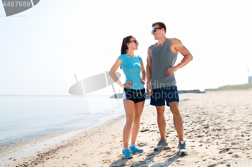 Image of happy couple in sports clothes and shades on beach