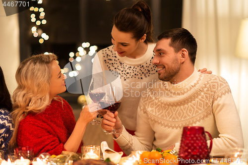 Image of happy friends drinking red wine at christmas party