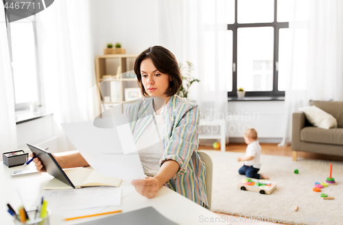 Image of working mother with tablet pc and papers at home