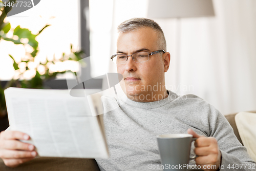 Image of man reading newspaper and drinking coffee at home