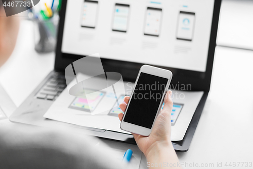 Image of web designer with smartphone and laptop at office