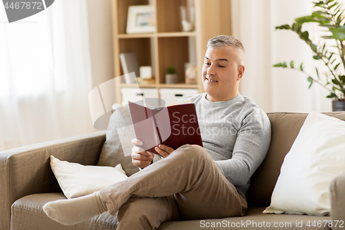 Image of man sitting on sofa and reading book at home