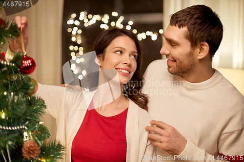 Image of happy couple decorating christmas tree at home