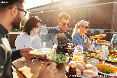 Image of happy friends eating at barbecue party on rooftop