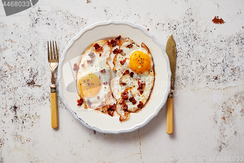 Image of Two fresh fried eggs with crunchy crisp bacon and chive served on rustic plate