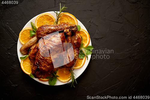 Image of Roasted whole chicken or turkey served in white ceramic plate with oranges