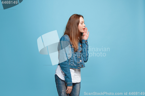 Image of The young teen girl whispering a secret behind her hand over blue background