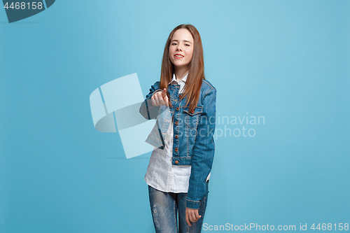 Image of The happy teen girl pointing to you, half length closeup portrait on blue background.