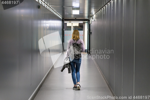 Image of Rear view of a casual female traveler walking narrow an airport corridor.