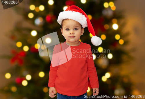 Image of baby girl in santa hat over christmas tree lights