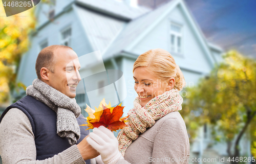 Image of smiling couple with autumn maple leaves over house