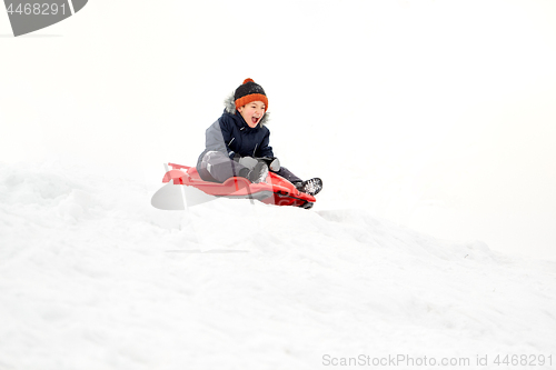 Image of happy boy sliding on sled down snow hill in winter