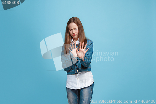 Image of Doubtful pensive teen girl rejecting something against blue background