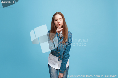 Image of The young teen girl whispering a secret behind her hand over blue background