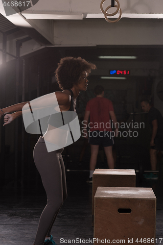 Image of black female athlete is performing box jumps at gym