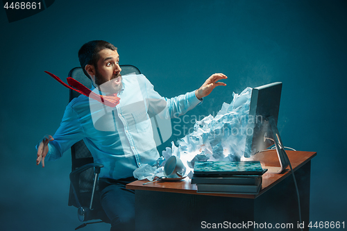 Image of Young stressed handsome businessman working at desk in modern office shouting at laptop screen and being angry about spam