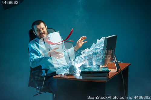 Image of Young stressed handsome businessman working at desk in modern office shouting at laptop screen and being angry about spam