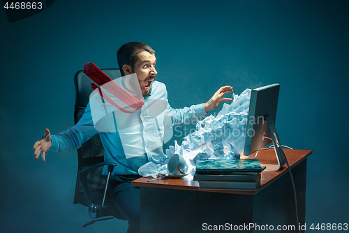 Image of Young stressed handsome businessman working at desk in modern office shouting at laptop screen and being angry about spam