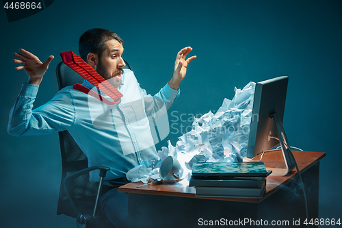 Image of Young stressed handsome businessman working at desk in modern office shouting at laptop screen and being angry about spam