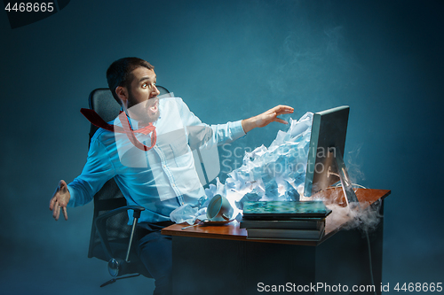 Image of Young stressed handsome businessman working at desk in modern office shouting at laptop screen and being angry about spam