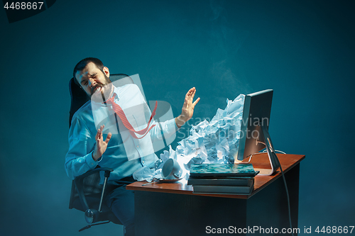 Image of Young stressed handsome businessman working at desk in modern office shouting at laptop screen and being angry about spam