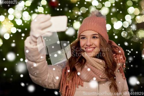 Image of young woman taking selfie over christmas tree