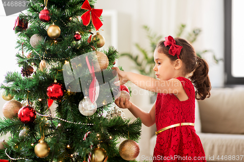 Image of little girl decorating christmas tree at home