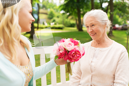 Image of daughter giving flowers to senior mother at park